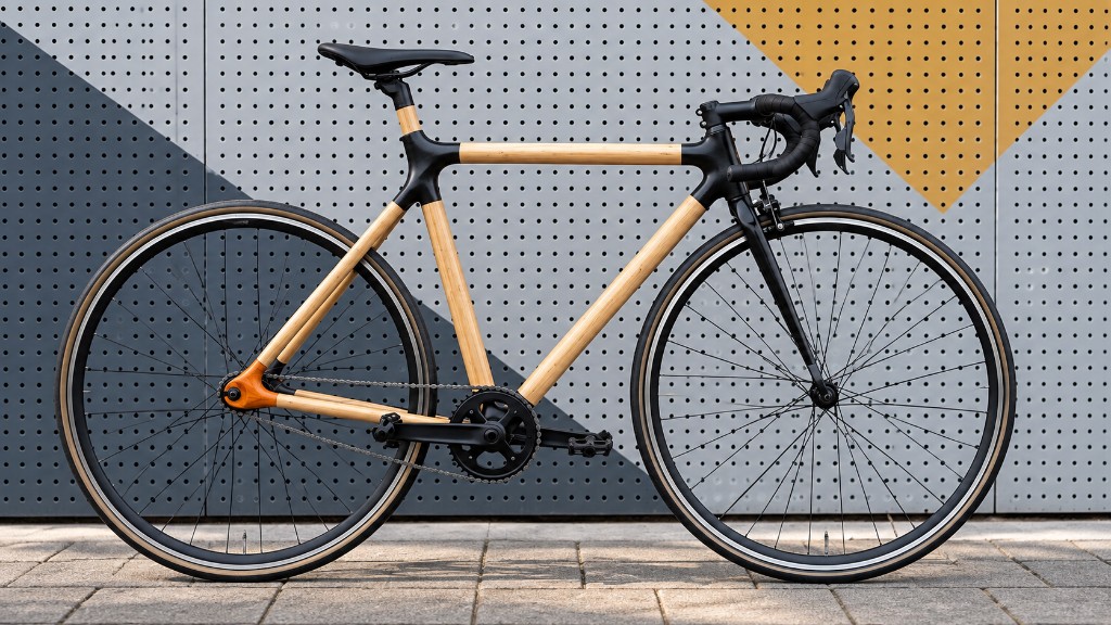 Side view of an Openframe bicycle with wooden tubes and black 3D-printed joints, in front of a perforated wall.