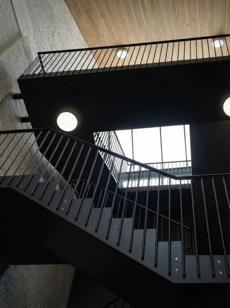 Black steel stair seen from below, with rod railings, round lamps and a roof light.