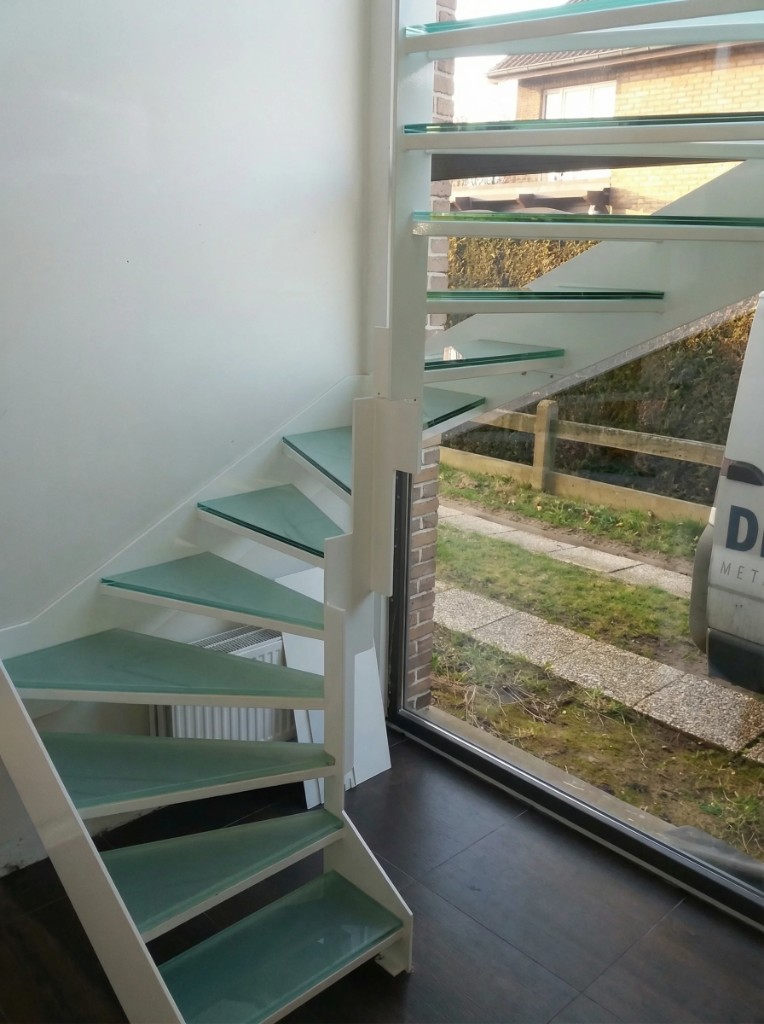 White steel stair with glass treads beside a large window.